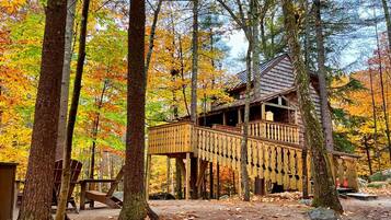 A wooden cabin with a deck, surrounded by trees with autumn foliage.
