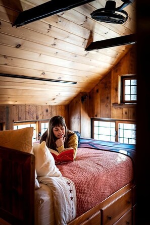 A wooden cabin interior with a bed, a window, and a ceiling fan.
