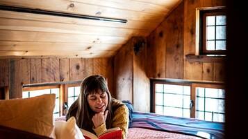 A wooden cabin interior with a bed, a window, and a ceiling fan.