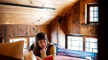 A wooden cabin interior with a bed, a window, and a ceiling fan.