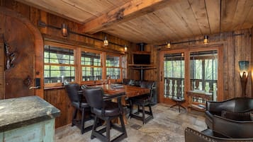 A rustic wooden interior with a dining table, chairs, and large windows.