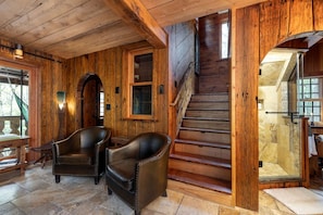 Un interior de madera con una escalera, sillones de cuero y suelo de piedra.