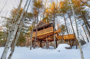 A wooden cabin with multiple levels, surrounded by trees and snow.