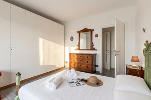 Ein Hotelzimmer mit einem Bett, einem Nachttisch mit Lampe, einem Holzkonsolenmöbel, einem Spiegel und einer Tür.