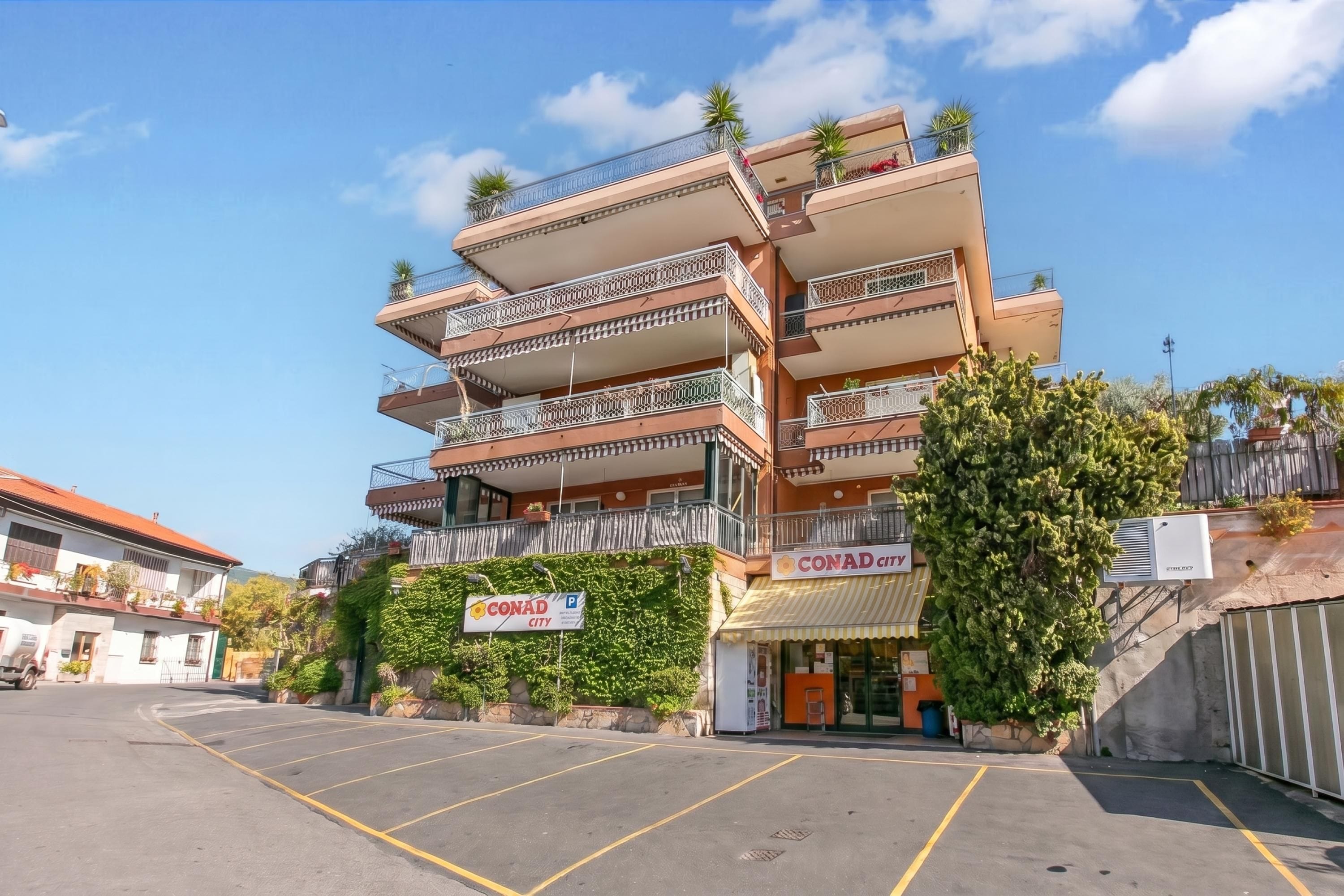 Un hôtel à plusieurs étages doté de balcons, d’un parking et d’une enseigne indiquant « CONAD CITY ».