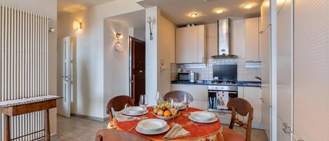 A dining area with a table set for four, a kitchen in the background, and a sliding door leading to another room.