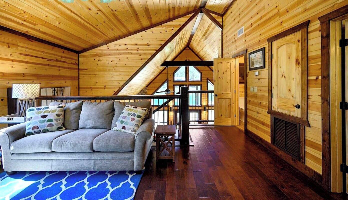 A cozy room with a wooden ceiling, a sofa with cushions, a small table, and a window with a view.