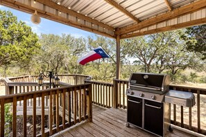 A covered outdoor deck with a grill, wooden railings, and a Texas flag.