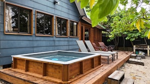 A wooden deck with a hot tub, lounge chairs, and a wooden deck extending from a house with large windows. - Fare Vainina (Moorea-Maiao)
