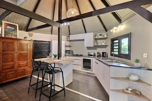 A modern kitchen with a central island, bar stools, and a wooden cabinet. - Fare Vainina (Moorea-Maiao)