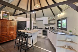 A modern kitchen with a central island, bar stools, a wooden cabinet, and a large window.
