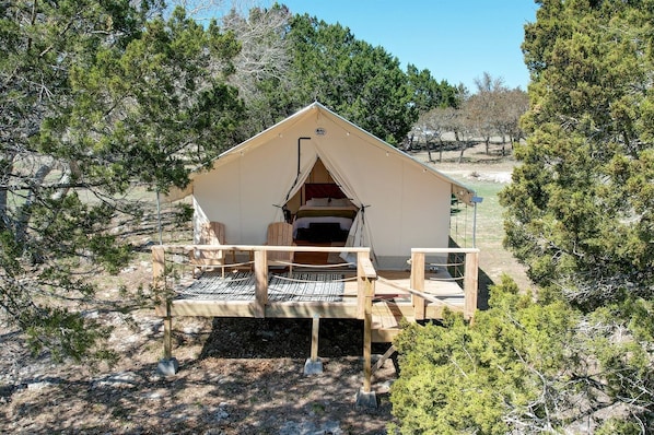 Una tienda de campaña con plataforma de madera, una cama en su interior y vistas a los árboles circundantes.