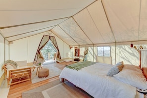 A tented accommodation with a bed, seating area, and a view of the outdoors.