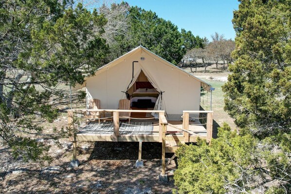 Une tente dotée d’une terrasse en bois, d’un lit à l’intérieur et offrant une vue sur les arbres environnants.