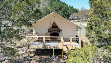 A tent with a wooden deck, a bed inside, and a view of the surrounding trees.