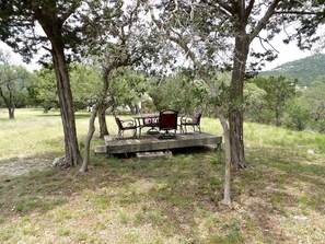 Un área de comedor al aire libre con una terraza de madera, sillas de metal y una mesa central.