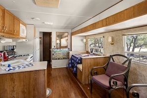 A compact kitchen with wooden cabinets, a sink, a stove, and a window with a view of trees.