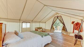 A tented accommodation with a bed, a small table, and a chair.