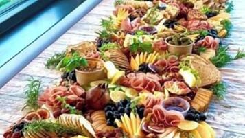 Uma tábua de frios com diversos queijos, carnes e frutas sobre uma mesa de madeira.