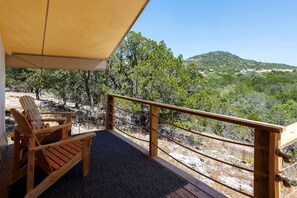 Una terraza de madera con una mesa y sillas, un toldo amarillo y vistas a un paisaje montañoso.