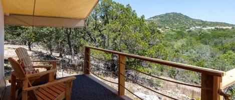 Una terraza de madera con una mesa y sillas, un toldo amarillo y vistas a un paisaje montañoso.