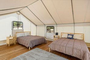 Alojamiento con tienda de campaña, dos camas, suelo de madera y ventanas.