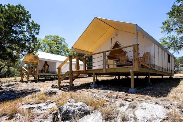 Une série de cabanes en bois, surmontées de toits en toile, nichées dans un paysage naturel et rocheux, avec des arbres en arrière-plan.