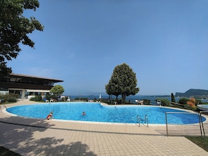 A swimming pool with a view of the sea, surrounded by a tiled deck and a building with a sloped roof. - CASA CATULLO, Paradise Children Apartment in Resort (Lombardia)