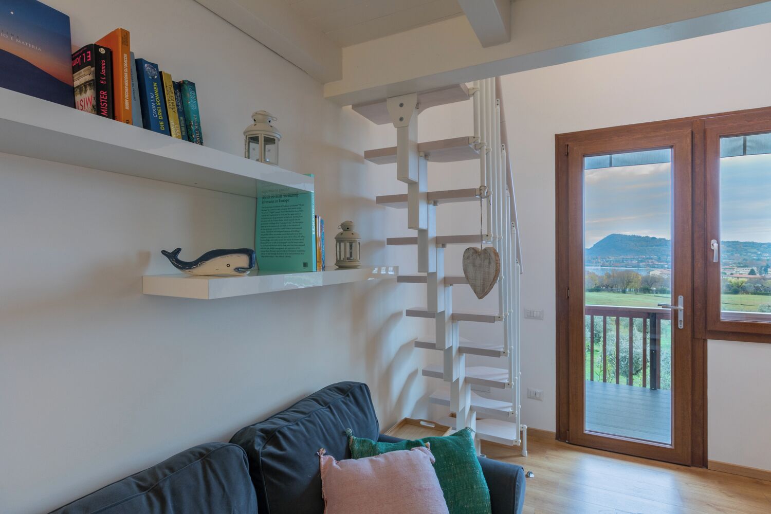 Un salon avec un canapé, une échelle blanche et une vue à travers une porte vitrée.
