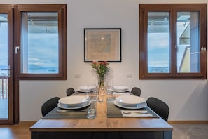 A dining table set with plates, glasses, and a vase of flowers, flanked by windows with a view of the sea and a framed map on the wall. - CASA CATULLO, Paradise Children Apartment in Resort (Lombardia)