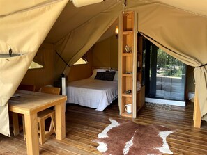 Un hébergement sous tente comprenant un lit, des meubles en bois, une étagère et une vue à travers une porte vitrée.