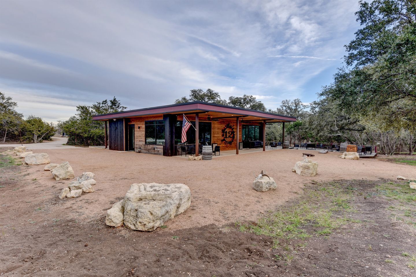 A rustic building with a covered patio, large rocks in the foreground, and a flag.