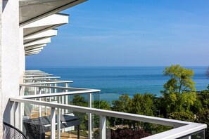 Ein Balkon mit freiem Blick auf das Meer, Gartenmöbel und üppiger Bepflanzung.