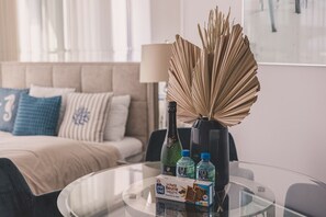 Ein Hotelzimmer mit Glastisch, einer Flasche, Pralinenschachtel und einer Zimmerpflanze.