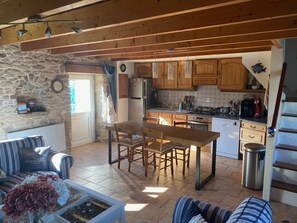 Eine gemütliche Küche mit Holzschränken, einem Essbereich mit Tisch und Stühlen, einer Steinwand und Blick ins Freie.