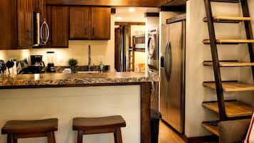 Una cocina con armarios de madera, electrodomésticos de acero inoxidable, encimera de granito y estantería tipo escalera.
