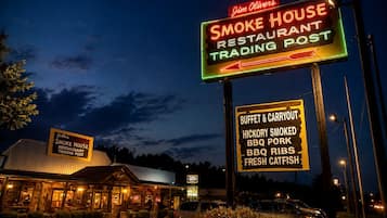 A restaurant with a neon sign indicating it is a smoke house and trading post, featuring a buffet and carryout, hickory smoked BBQ, ribs, and fresh catfish.