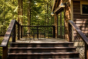 Une terrasse en bois dotée d’une rambarde, d’une table et de chaises, qui mène à un bâtiment aux grandes fenêtres.