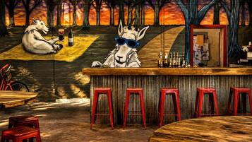 A bar with a mural of animals, red stools, and a wooden bar counter.