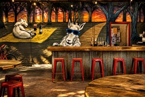 Un bar con un mural de animales, taburetes rojos y una barra de madera.