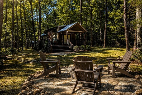 Une cabane avec une véranda, entourée d’une forêt. On y trouve deux fauteuils Adirondack devant l’entrée.