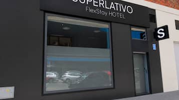 Un bâtiment moderne avec une enseigne indiquant « SUPERLATIVO FlexStay HOTEL » et une grande fenêtre qui reflète les voitures garées.