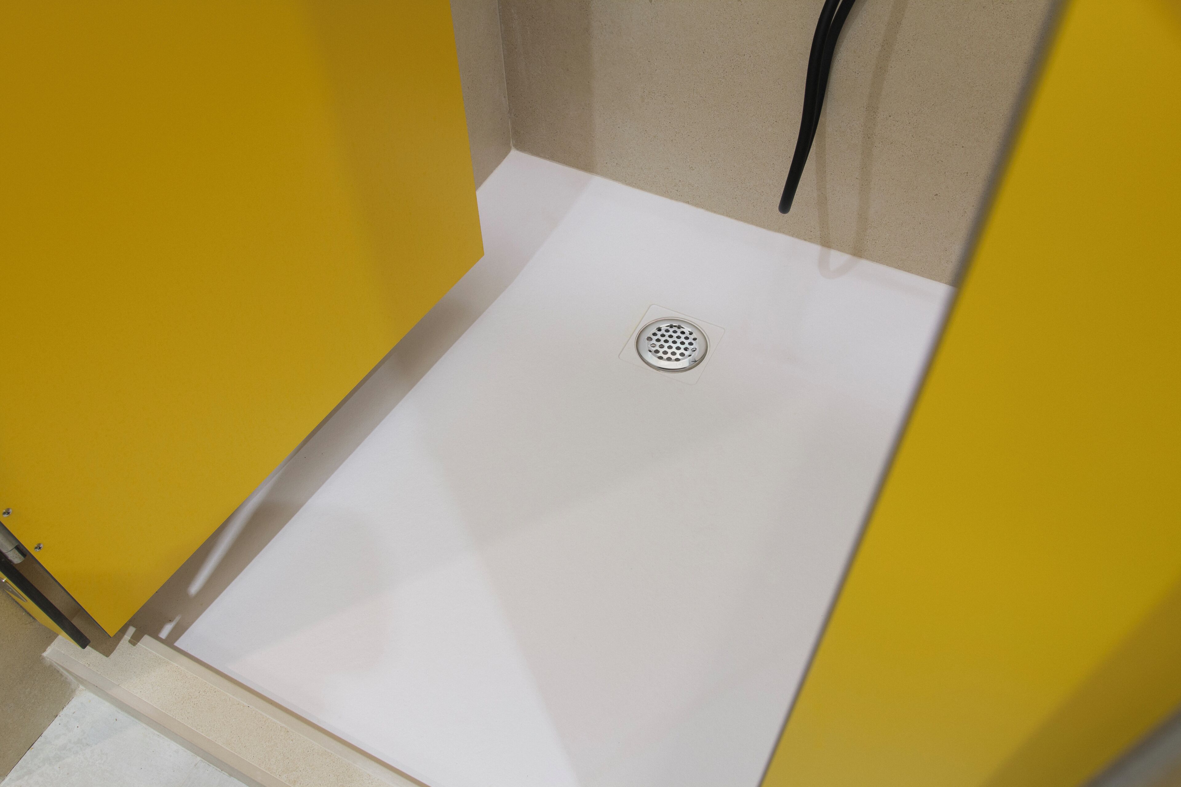 A white shower with a drain, yellow walls, and a beige floor.