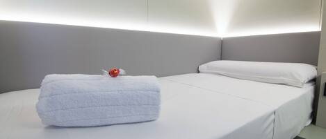 Una cama bien hecha con una toalla blanca y un adorno rojo, un cabecero gris y una pared blanca.