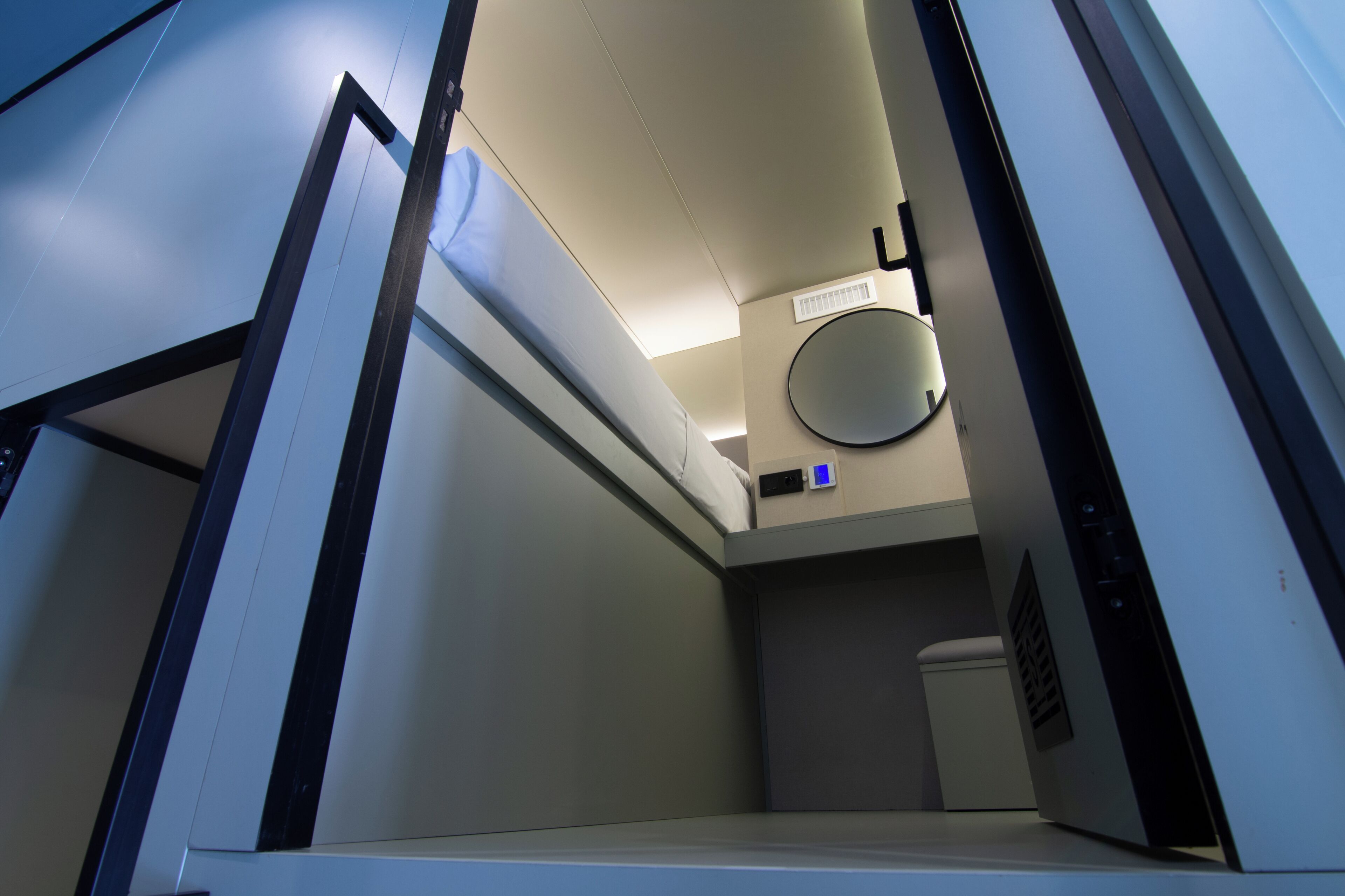A narrow hallway with a door leading to a room, a round mirror on the wall, and a small window.