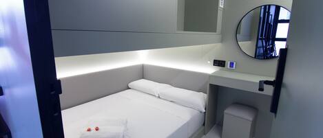 Una habitación de hotel moderna con una cama individual, una mesita de noche, un espejo y un taburete pequeño.