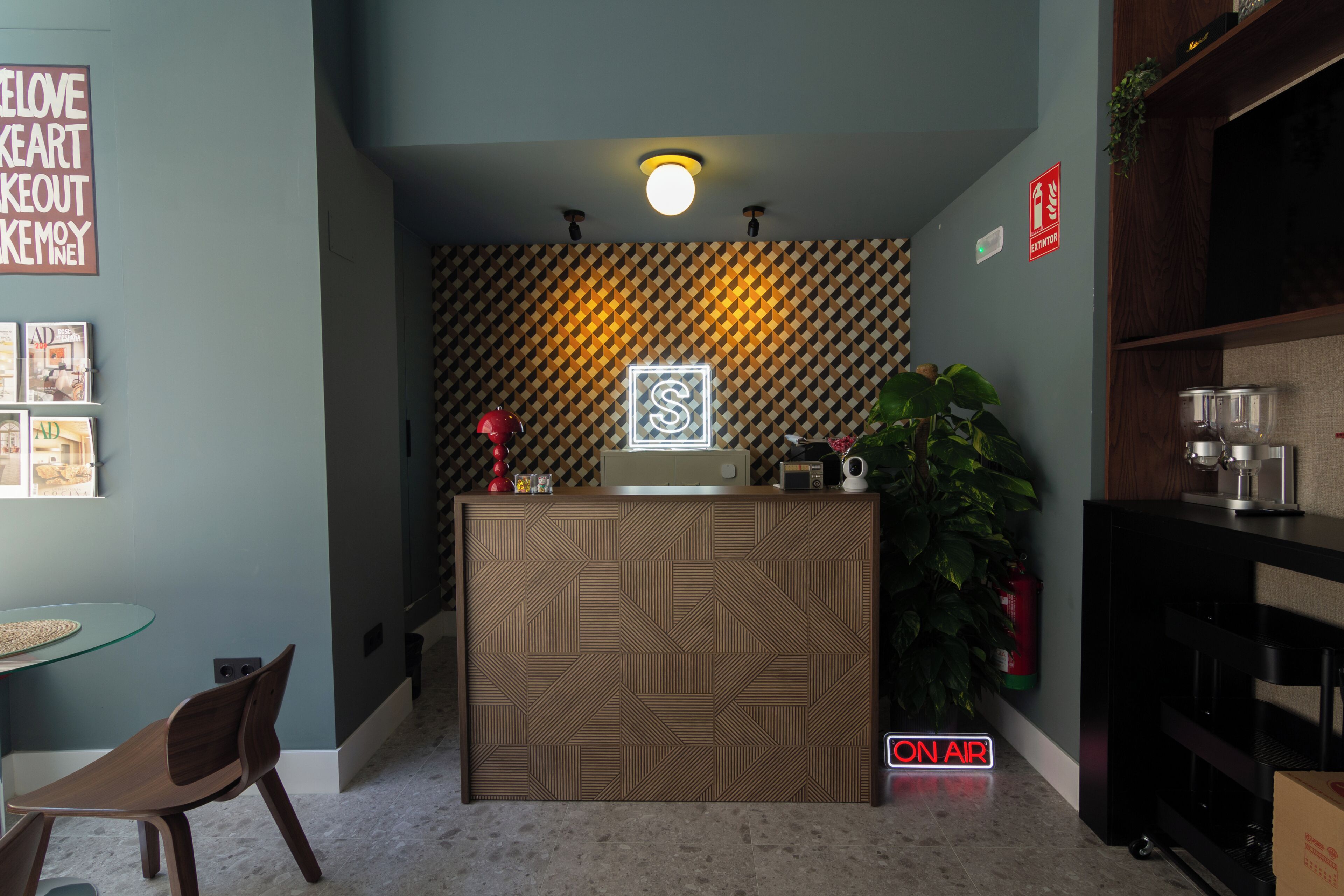 Zona de recepción con pared estampada, mostrador de recepción, máquina de café, planta y extintor.