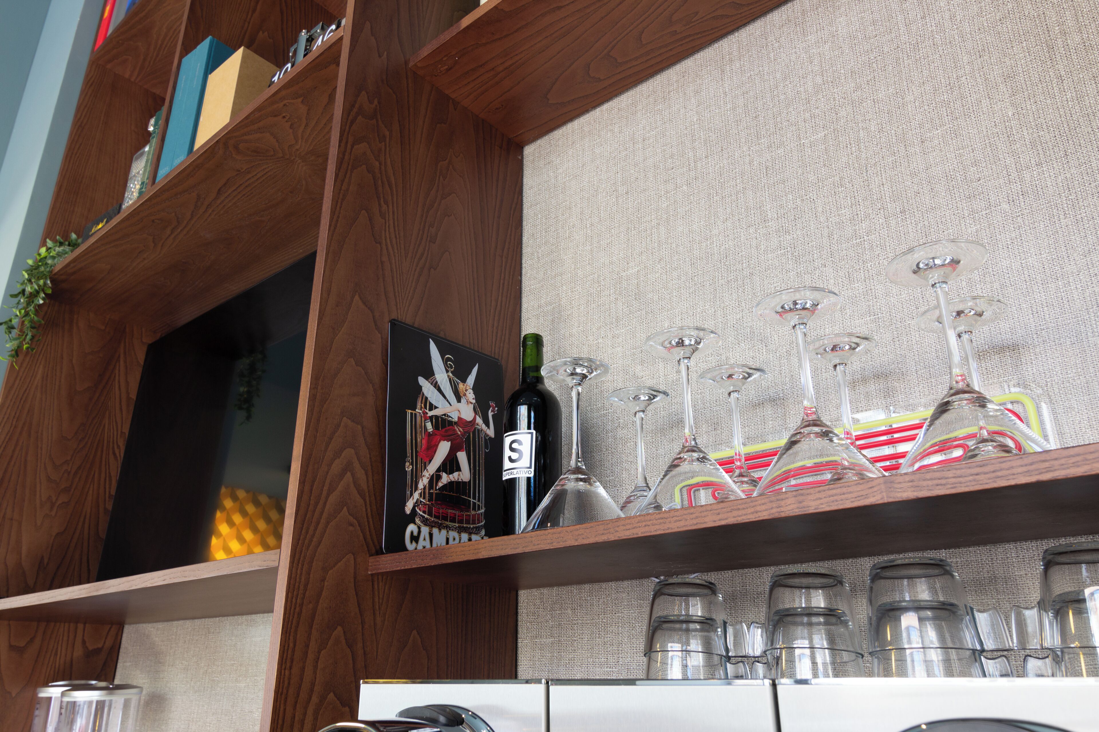 Une étagère en bois avec une bouteille de vin et des verres, un tableau encadré et une petite plante.