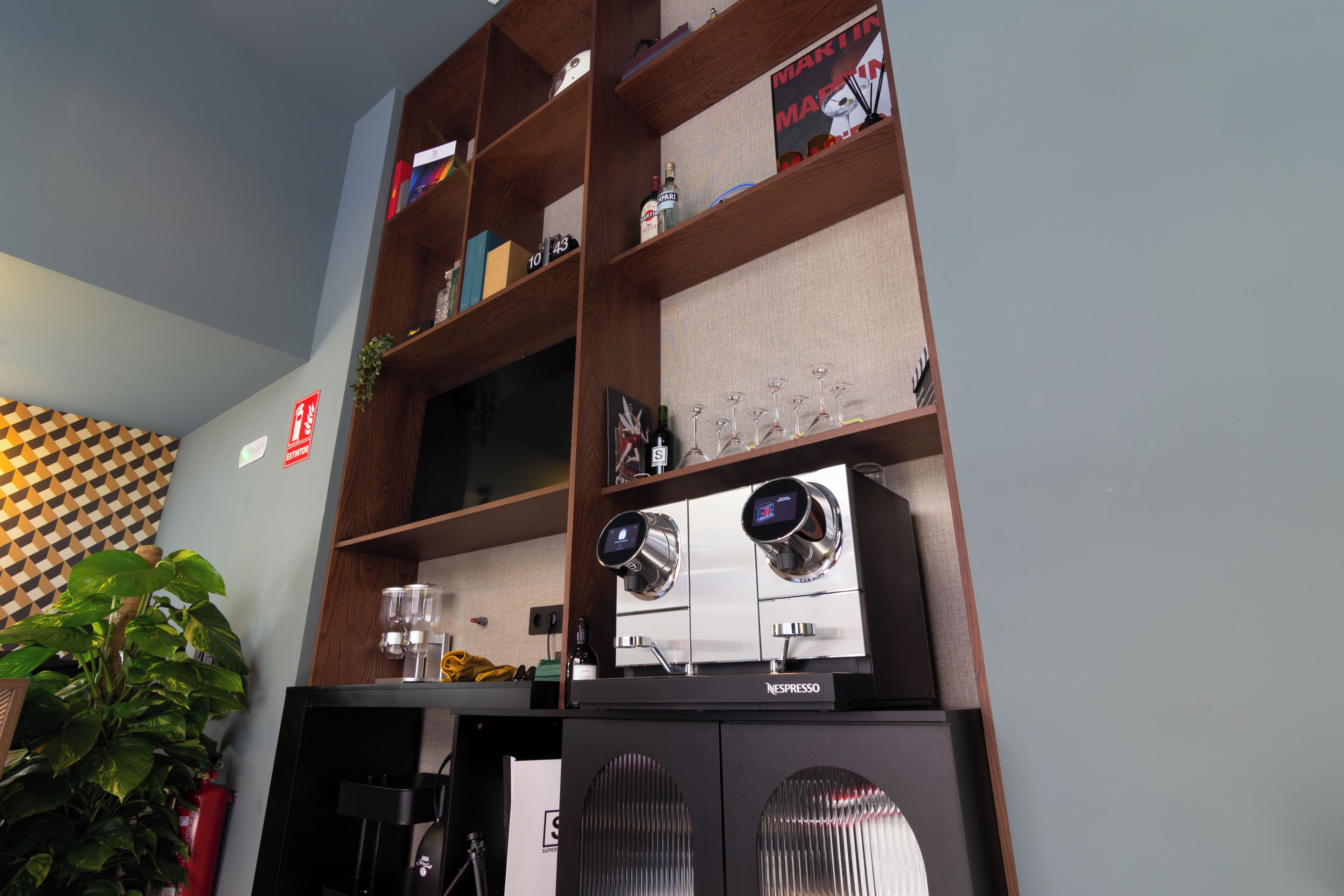 Une pièce équipée d’une machine à café, d’étagères remplies de livres et d’objets décoratifs, et d’une plante.