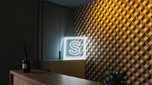 A reception desk with a geometric patterned wall, a neon sign, and a plant. - Hostel Superlativo Vialia I (Málaga)